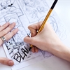 An artist's hand holding a pencil drawing a comic strip.