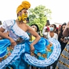 Two Black women in colorful dresses dance in front of a crowd to celebrate Juneteenth.