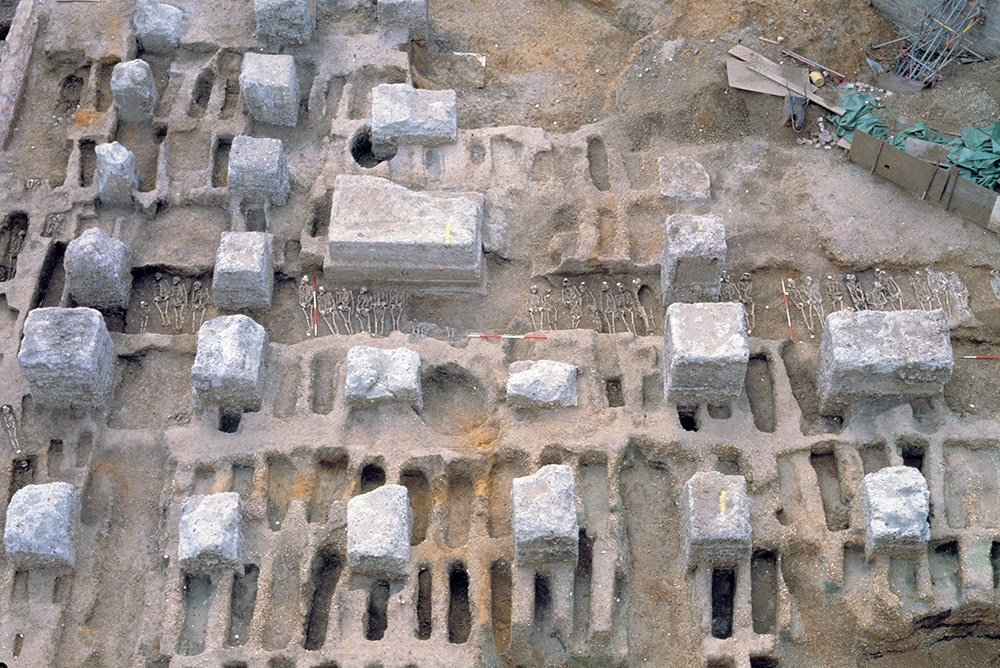 Overhead shot of a partially-excavated graveyard with skeletons visible.