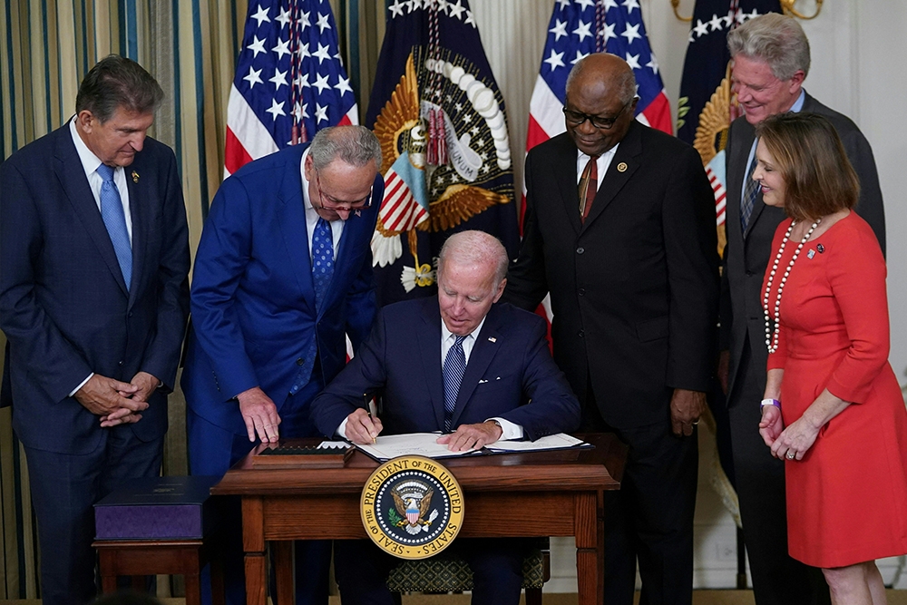 President Joe Biden signs the Inflation Reduction Act. From left to right: Senator Joe Manchin, Senator Chuck Schumer, President Joe Biden, Representative James Clyburn, Representative Frank Pallone, and Representative Kathy Castor.